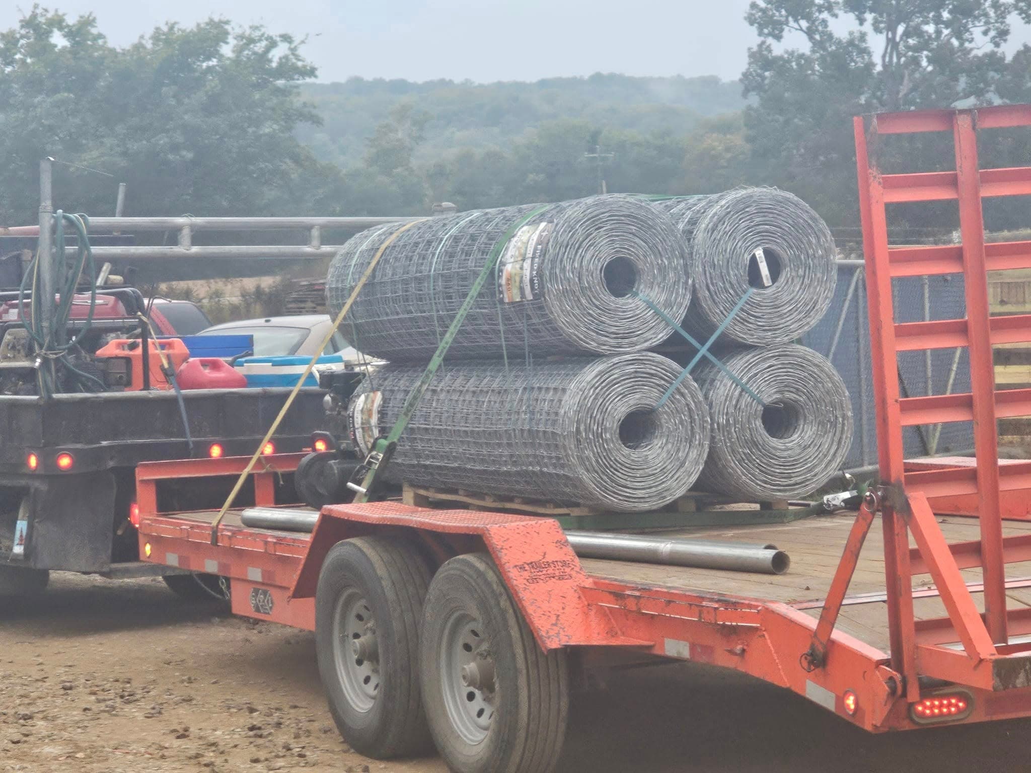 A flatbed trailer loaded with rolls of galvanized woven-wire field fencing ready for a farm job