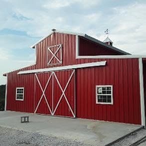 A custom-built red barn with white X-trim sliding doors and a gambrel roof on a rural property