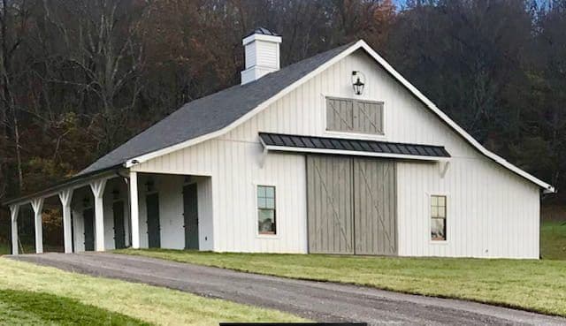 A custom white board-and-batten barn with a black accent roof, gray X-trim sliding doors, and a covered side lean-to
