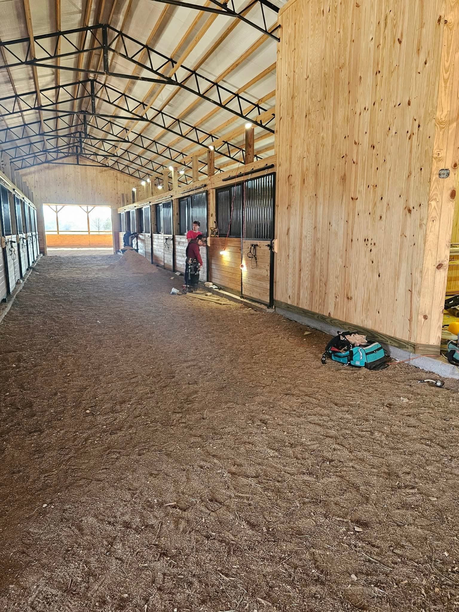 The interior aisle of a horse barn under construction with wood-lined stalls and steel grilles