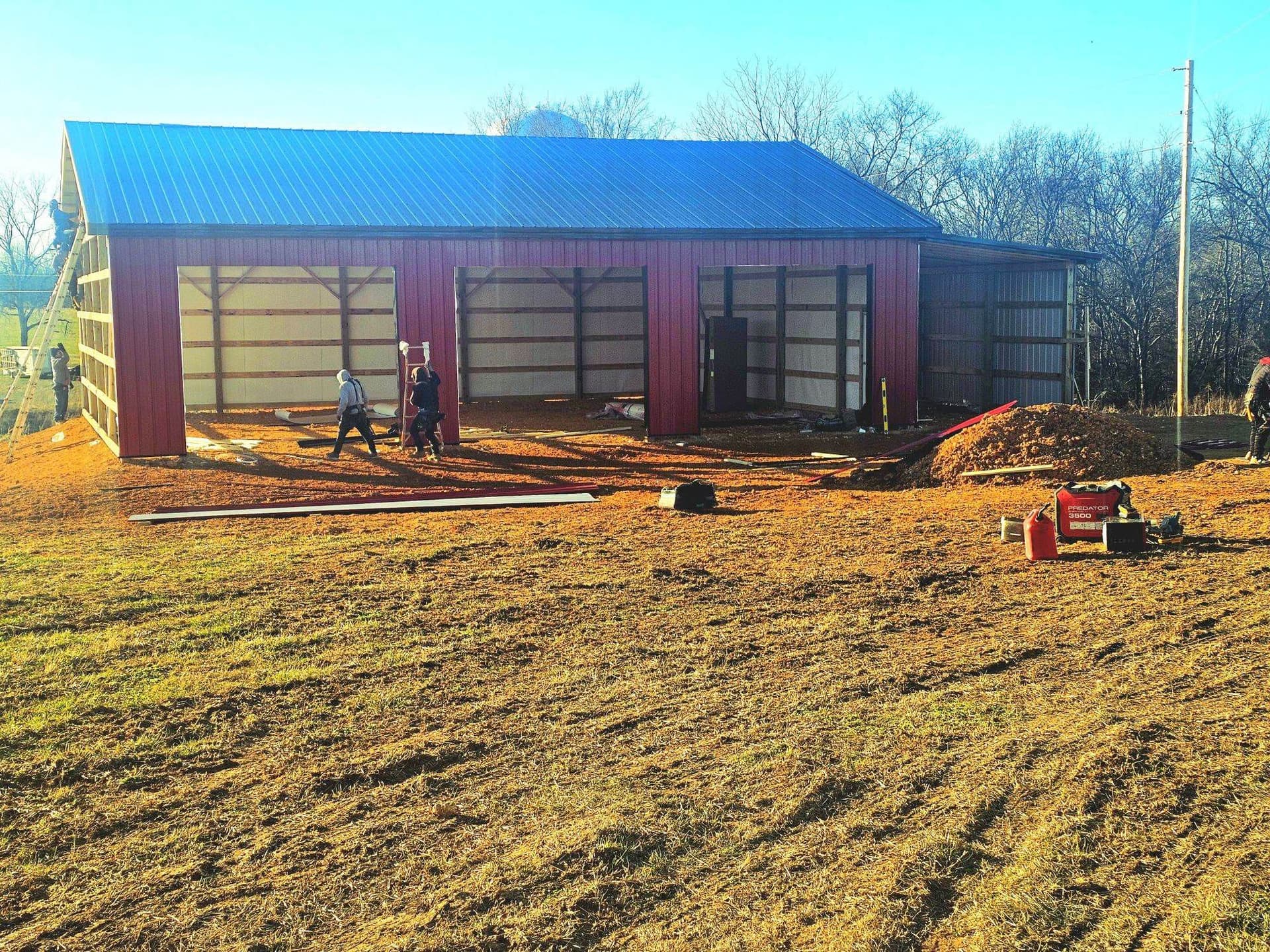 A red metal pole barn under construction on a rural property with a blue metal roof