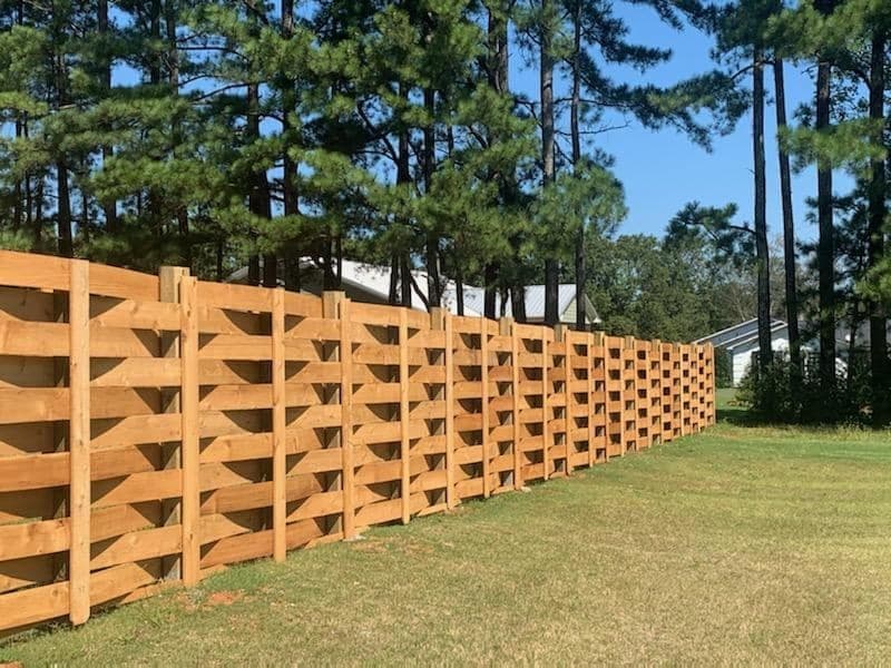A cedar privacy fence wrapping a landscaped backyard with a footbridge